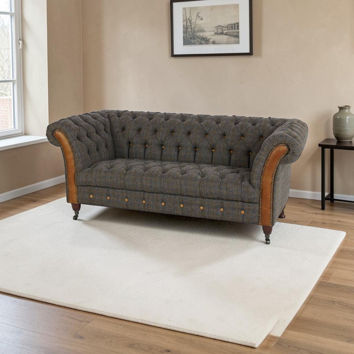 A classic Chesterfield-style loveseat sofa upholstered in textured Uist Harris Tweed with tan leather arm panels and brass button details, positioned on a cream area rug in a living room setting.