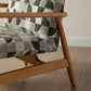 Close-up of a wooden chair with patterned fabric on a wooden floor.