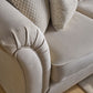 Close-up of a light beige upholstered sofa arm and seat cushion with two textured throw pillows, photographed indoors on a wood floor.