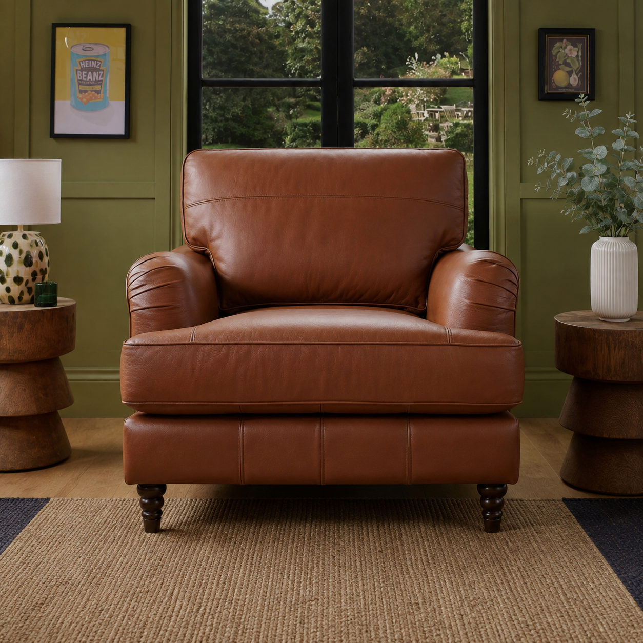 A brown leather armchair with rolled arms and dark turned legs, positioned in a styled living room setting with olive green walls, wooden side tables, and a window in the background.