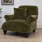 An olive green velvet armchair with a matching throw pillow, set in a room with light wood floors and white paneled walls.