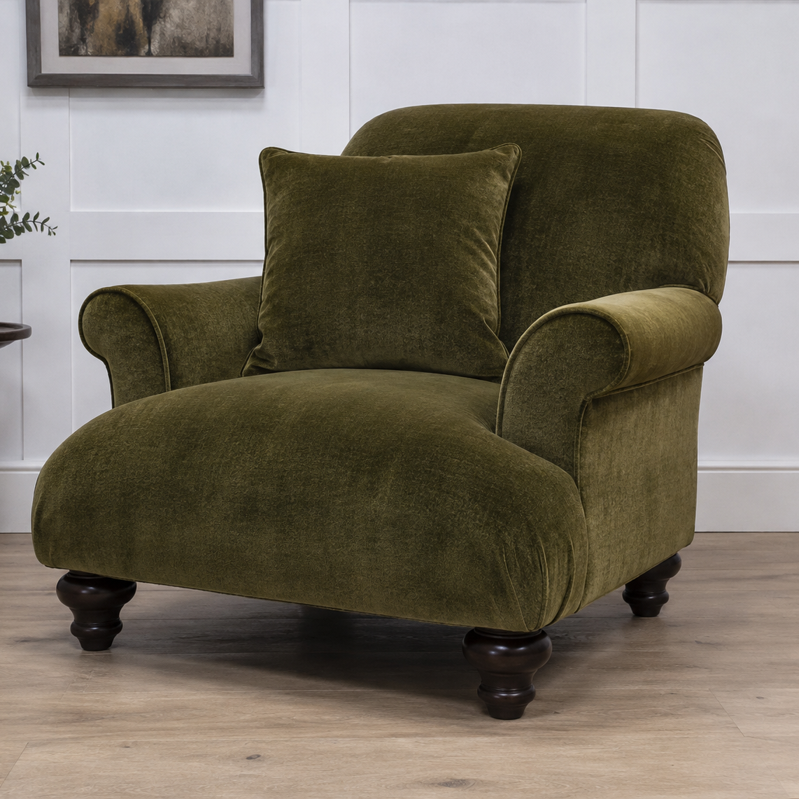 An olive green velvet armchair with a matching throw pillow, set in a room with light wood floors and white paneled walls.