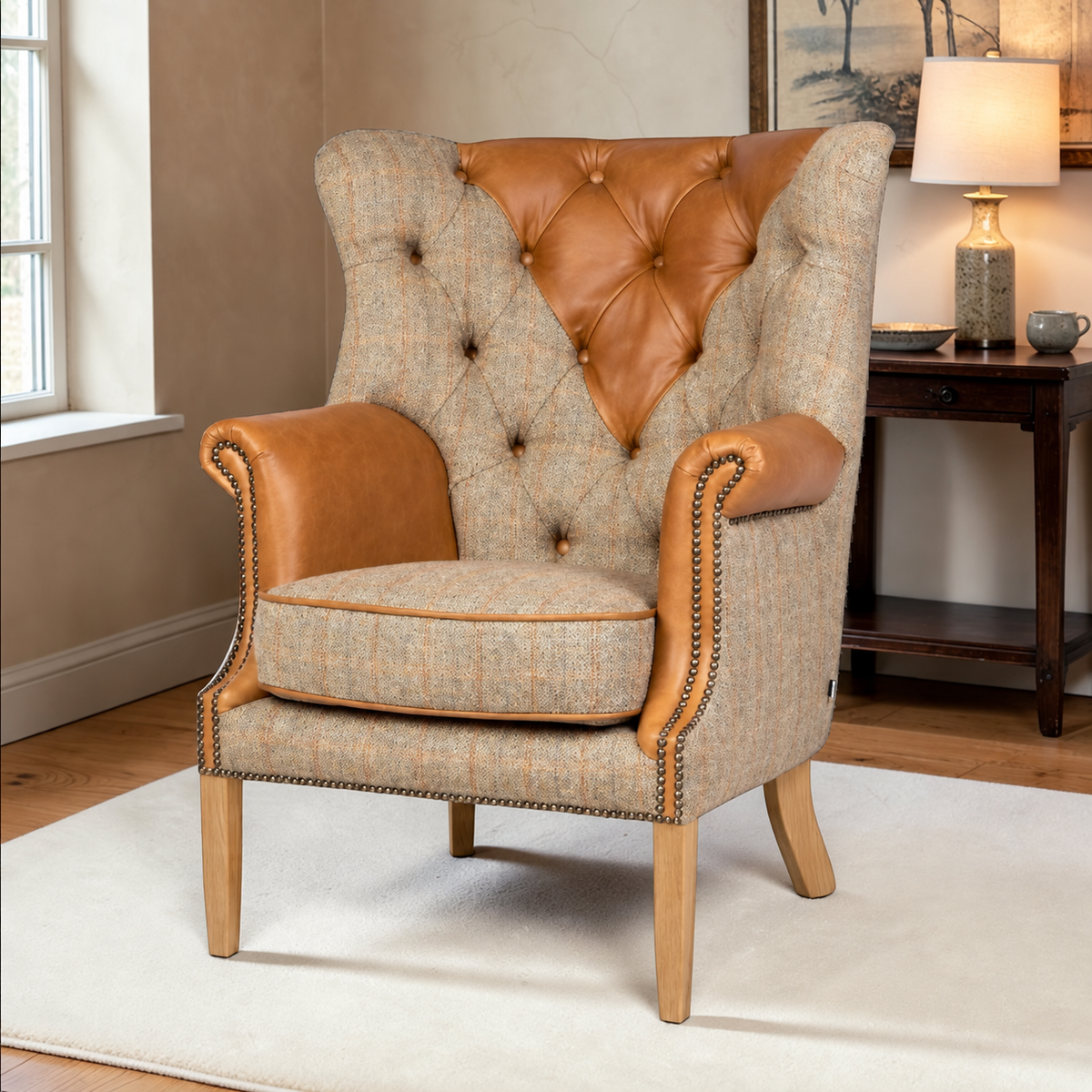 A classic wingback armchair with a beige and brown tweed fabric, tan leather tufted backrest and armrests, and light wood legs, shown in a styled living room setting.