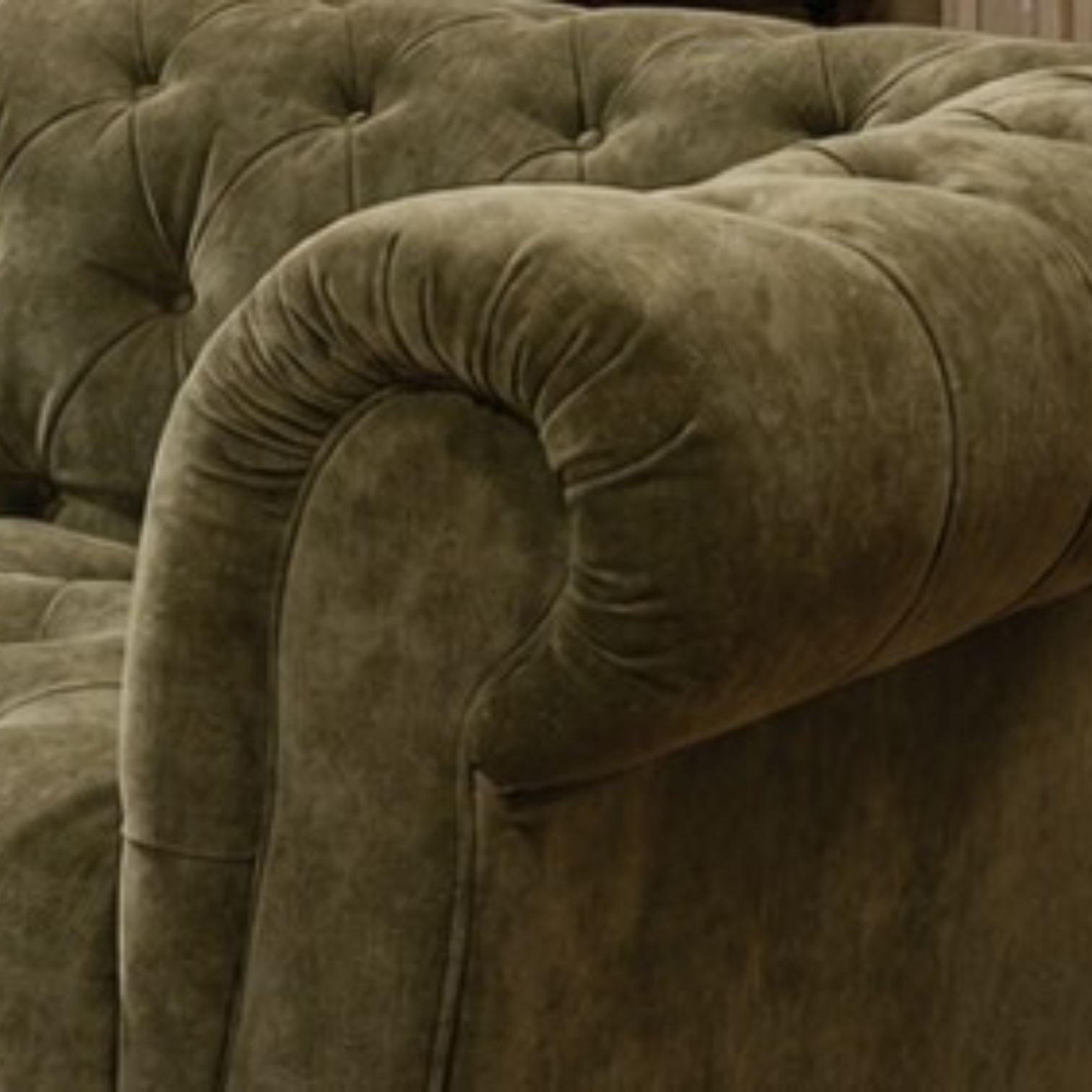 Close-up of a tufted velvet armchair in a muted olive green color, showing the plush fabric texture and rolled arm detail.