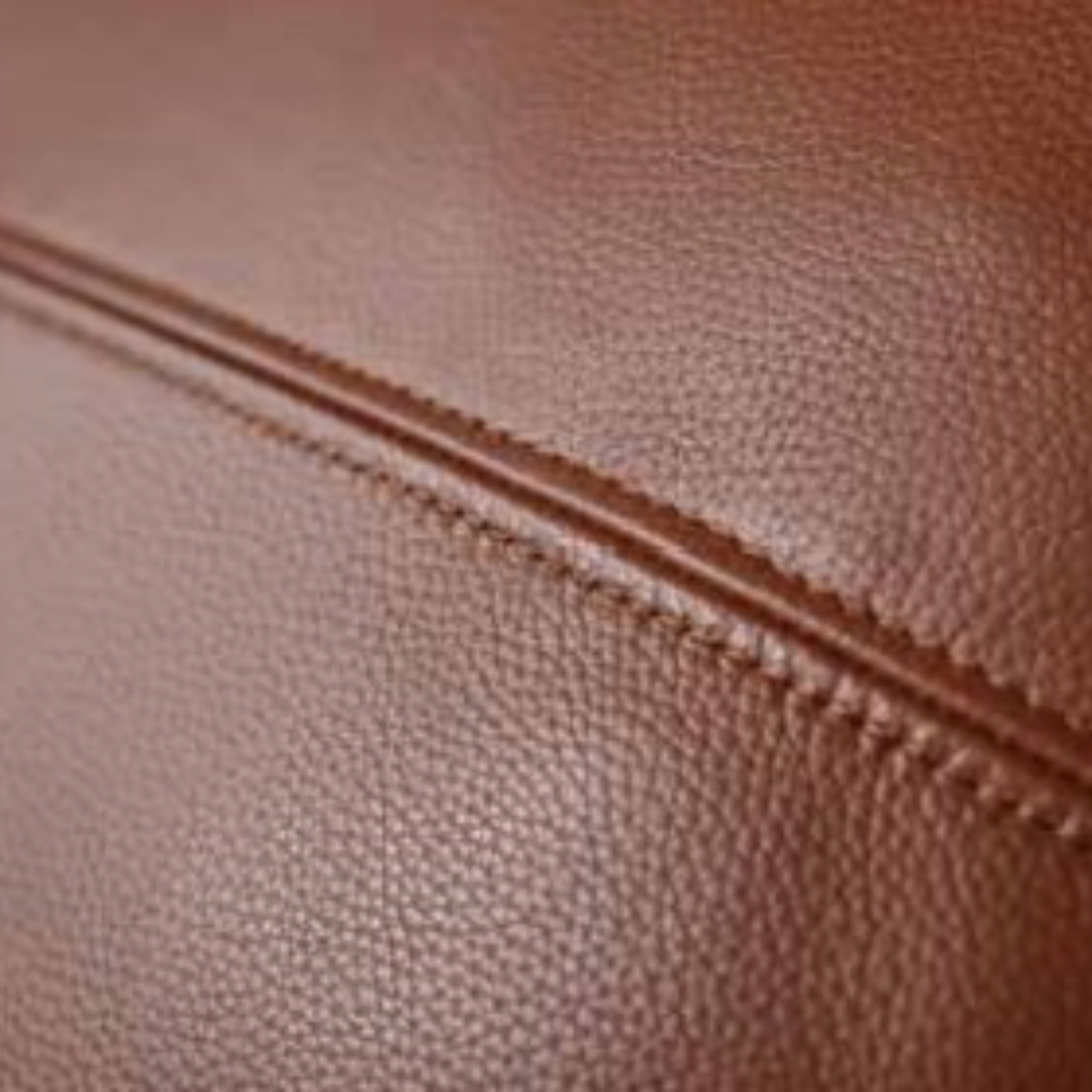 Close-up of a brown pebbled leather surface with a stitched seam running diagonally across the frame.