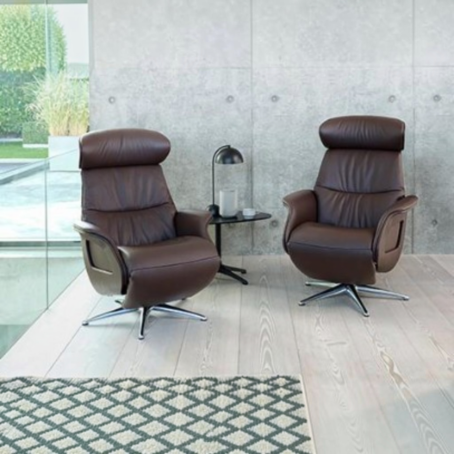 Two modern brown leather swivel recliner chairs with chrome bases, shown in a contemporary living room setting with a concrete wall, light wood flooring, and a small black side table between them.