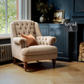 A tufted beige armchair with rolled arms and dark wooden legs sits in a styled room with a dark blue cabinet, wood floor, and a brown pillow. A 'letrad' brand overlay is visible on the right.