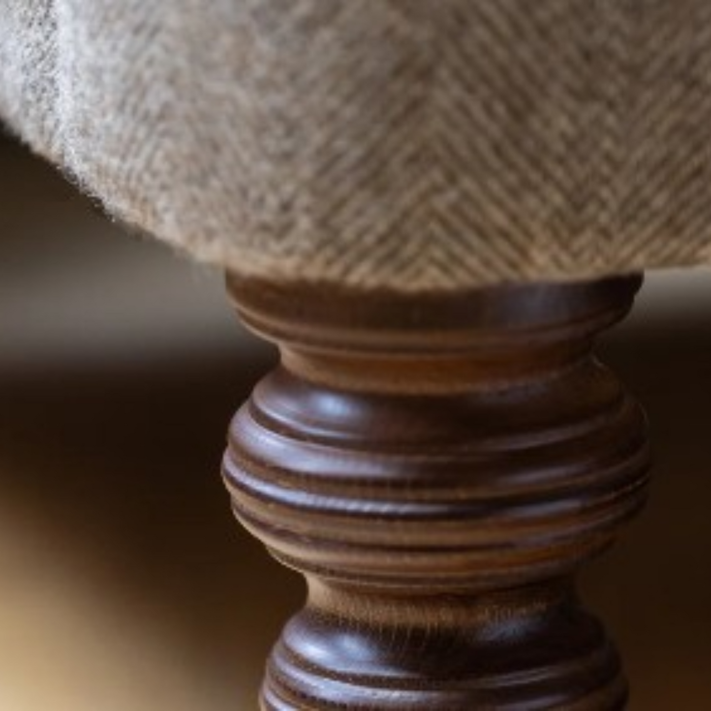 Close-up of a woven beige fabric cushion or upholstered top mounted on a dark brown ribbed wooden pedestal base.