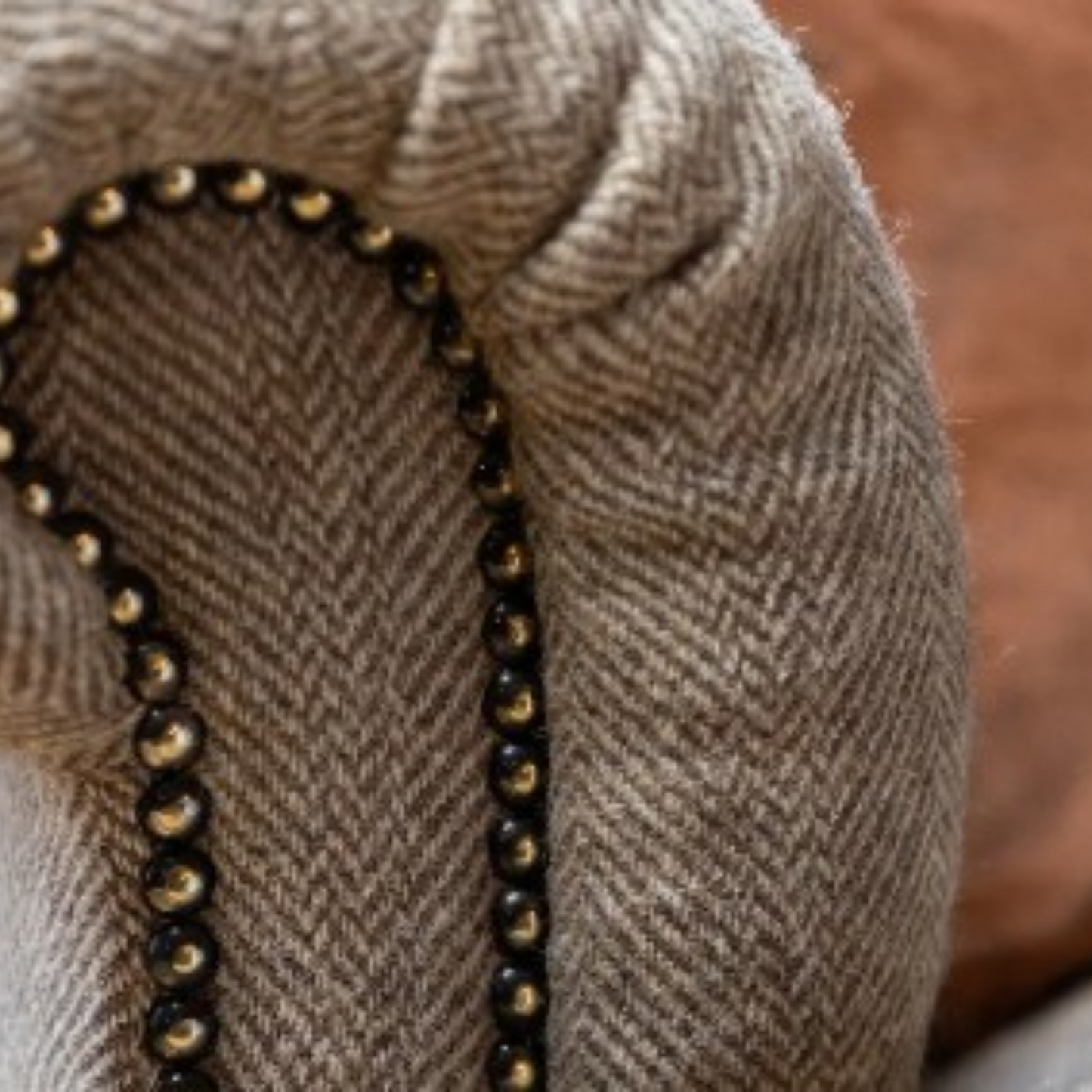 Close-up of a beige herringbone fabric with a curved border of black beads and small gold-toned accents.