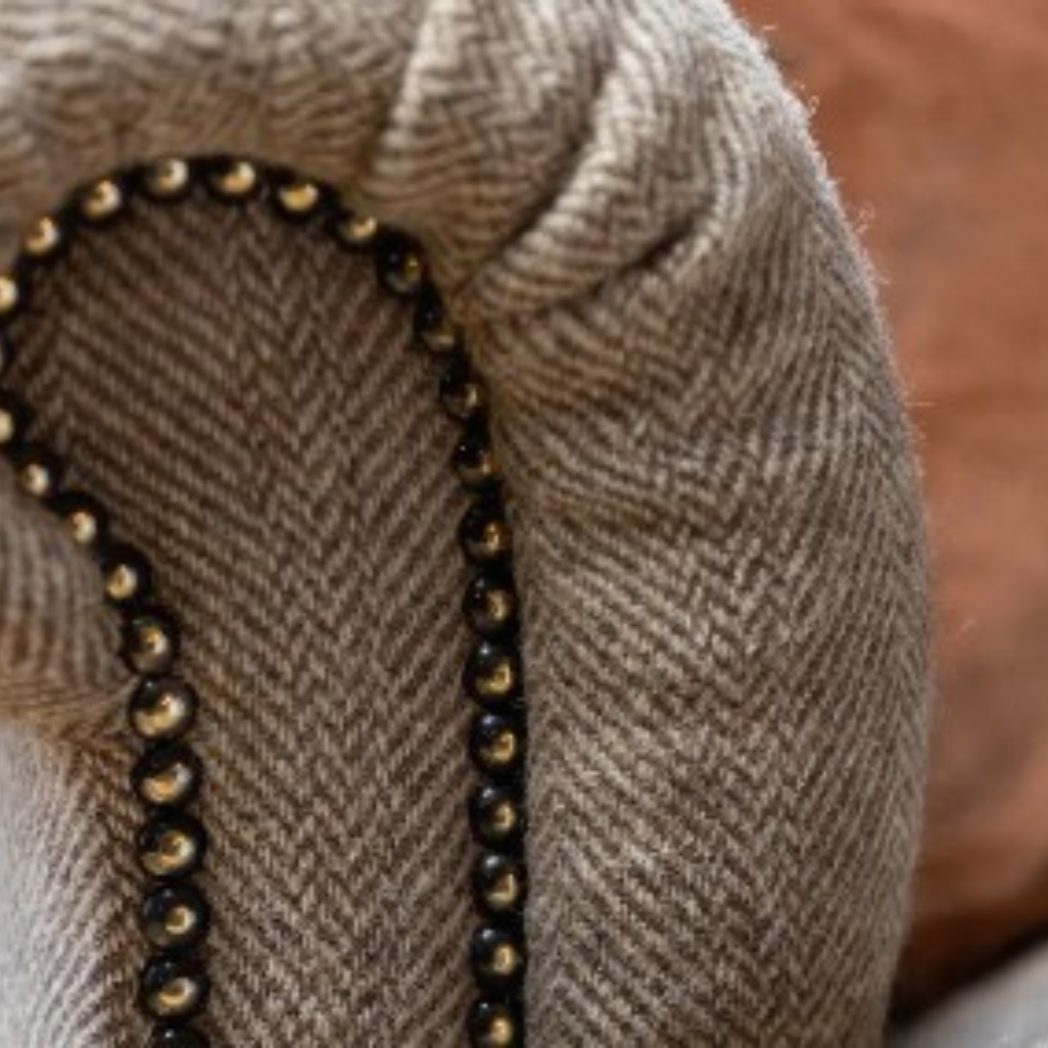 Close-up of a beige herringbone fabric with a curved border of black beads and small gold-toned accents.