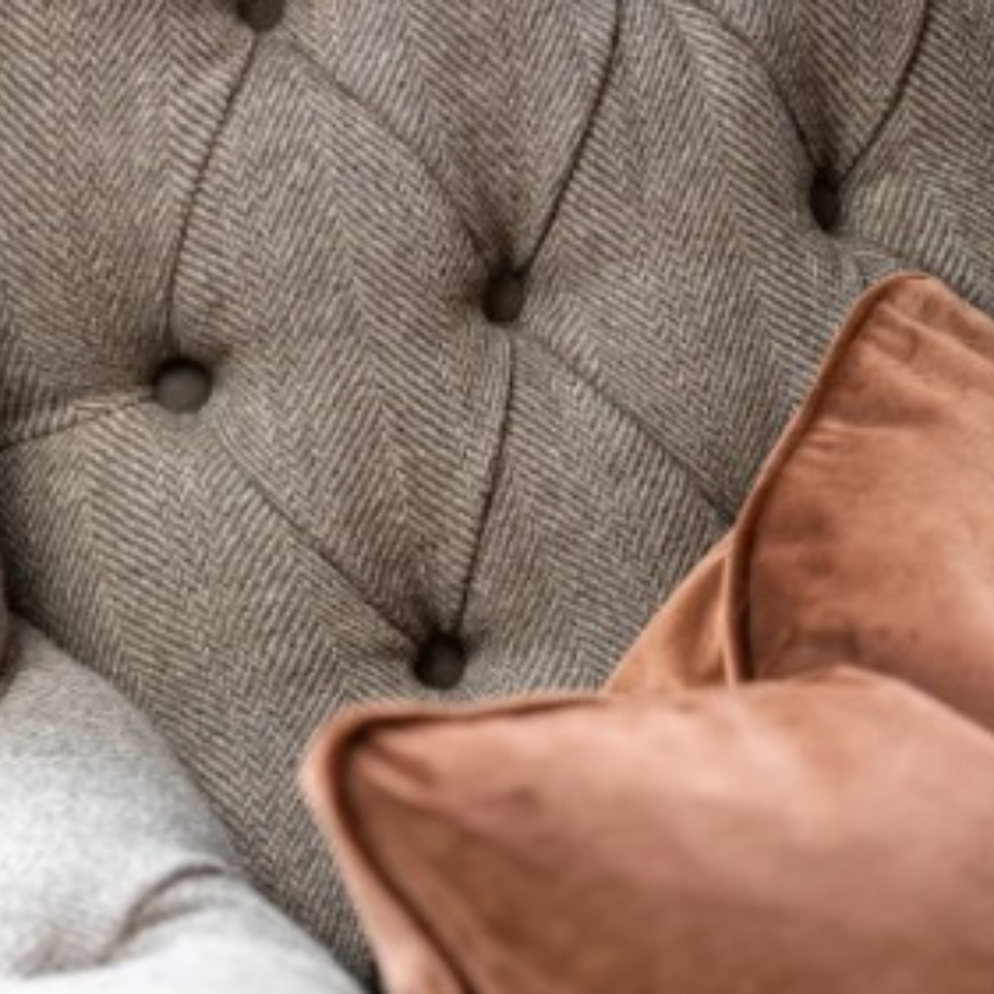 Close-up of a tufted armchair upholstered in gray herringbone fabric, with a dusty rose velvet throw pillow resting in the foreground.