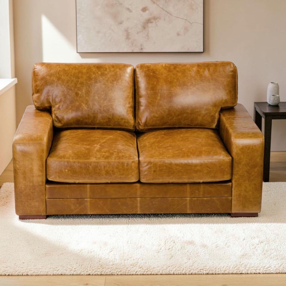 A two-seater sofa upholstered in distressed Cerato brown leather, positioned on a white shag rug in a living room setting with a side table and wall art in the background.