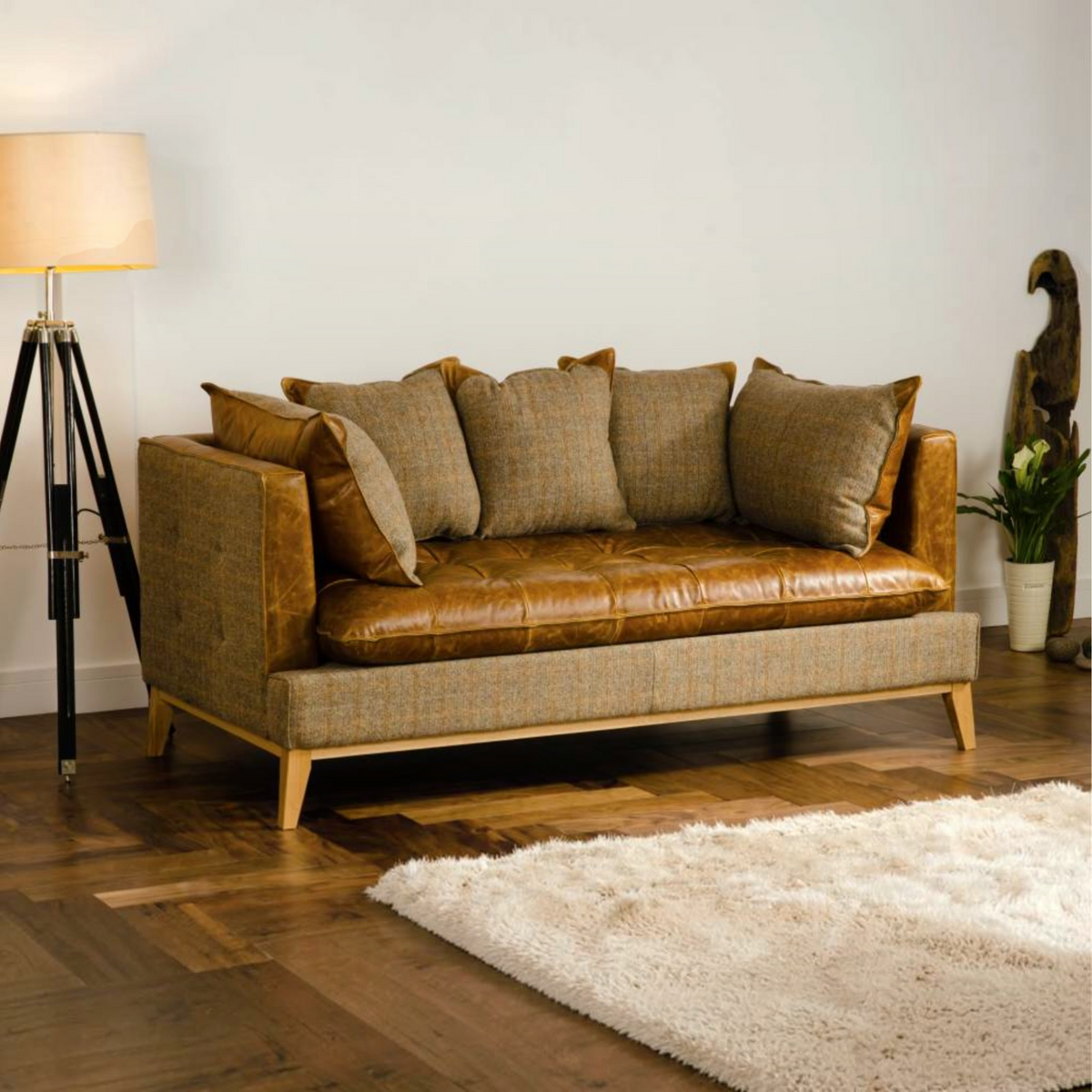 A three-seater sofa with Cerato brown leather seat and backrest, upholstered in a textured beige tweed fabric on the sides and arms, styled in a living room with a floor lamp, wooden floor, and white rug.
