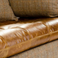 Close-up of a brown leather sofa cushion with tufting, next to a textured brown and beige herringbone wool pillow and matching sofa fabric.