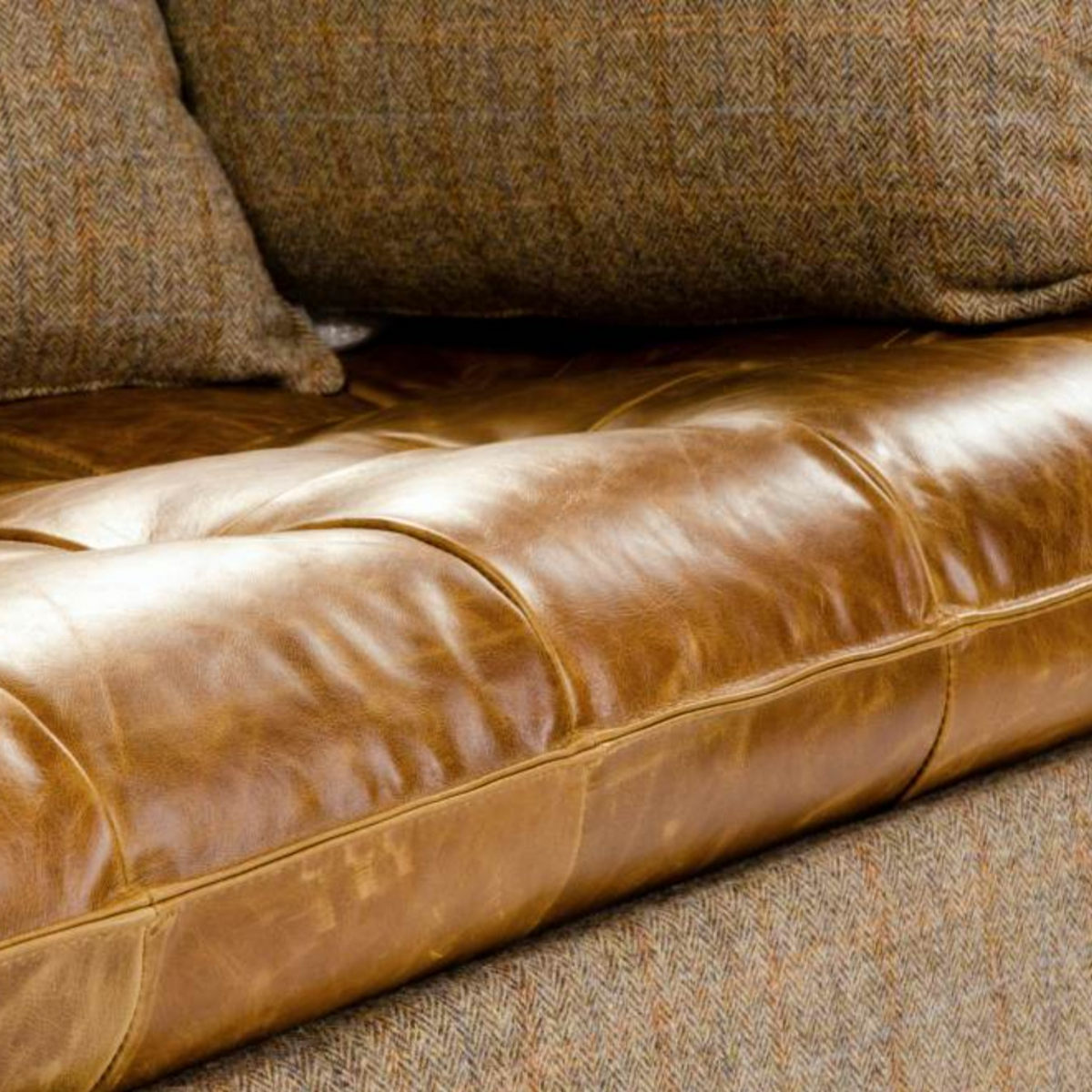 Close-up of a brown leather sofa cushion with tufting, next to a textured brown and beige herringbone wool pillow and matching sofa fabric.