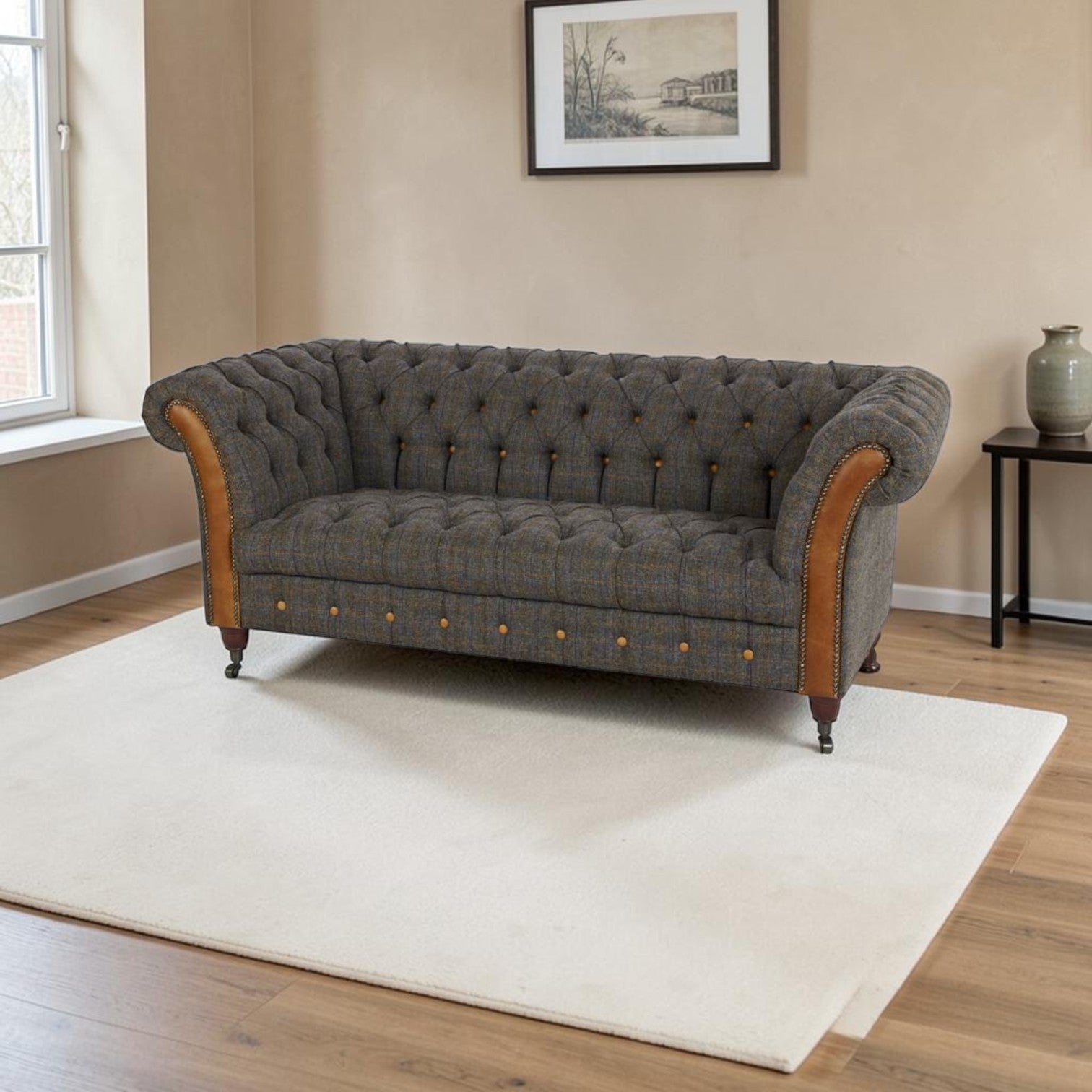 A classic Chesterfield-style loveseat sofa upholstered in textured Uist Harris Tweed with tan leather arm panels and brass button details, positioned on a cream area rug in a living room setting.