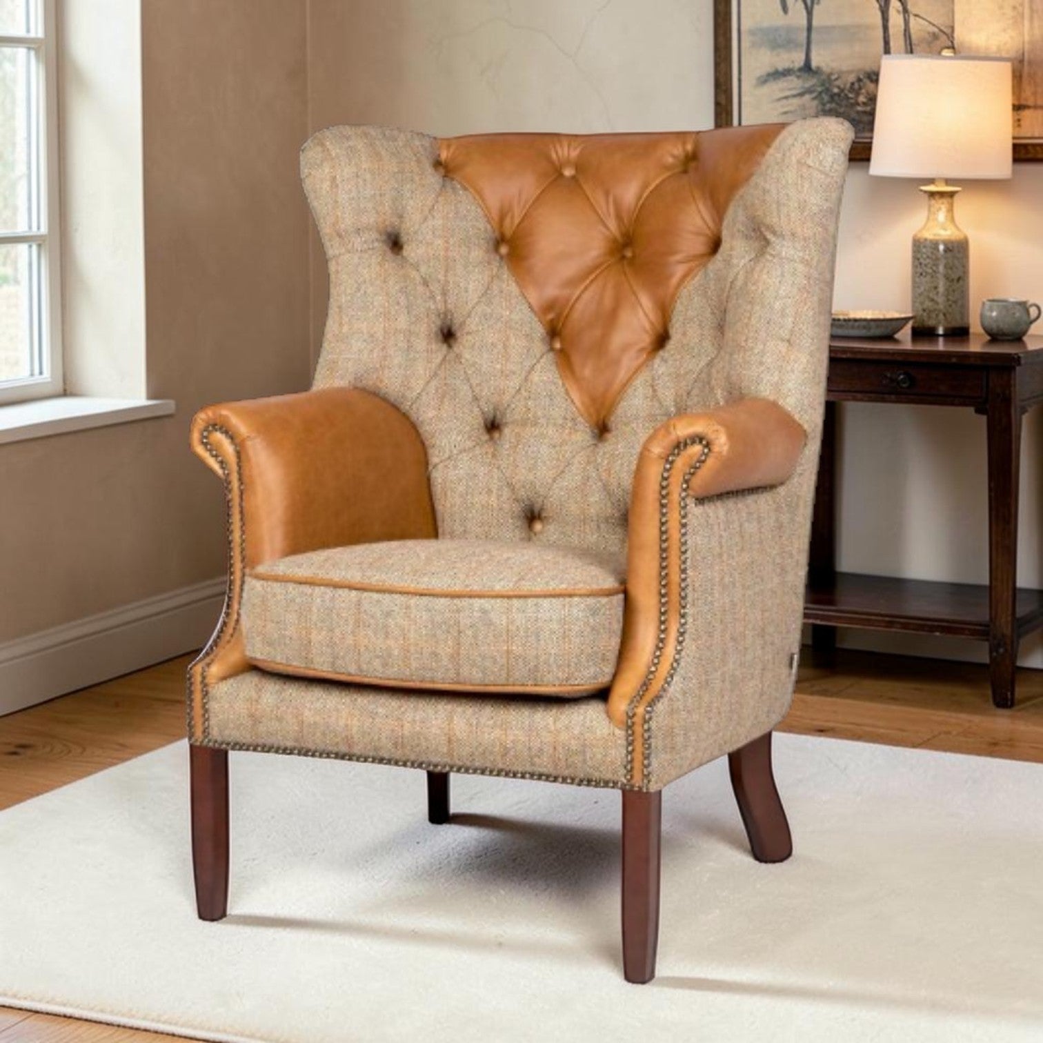 A classic wingback armchair with a beige and brown tweed fabric, tan leather tufted backrest and armrests, and dark wood legs, shown in a styled living room setting.