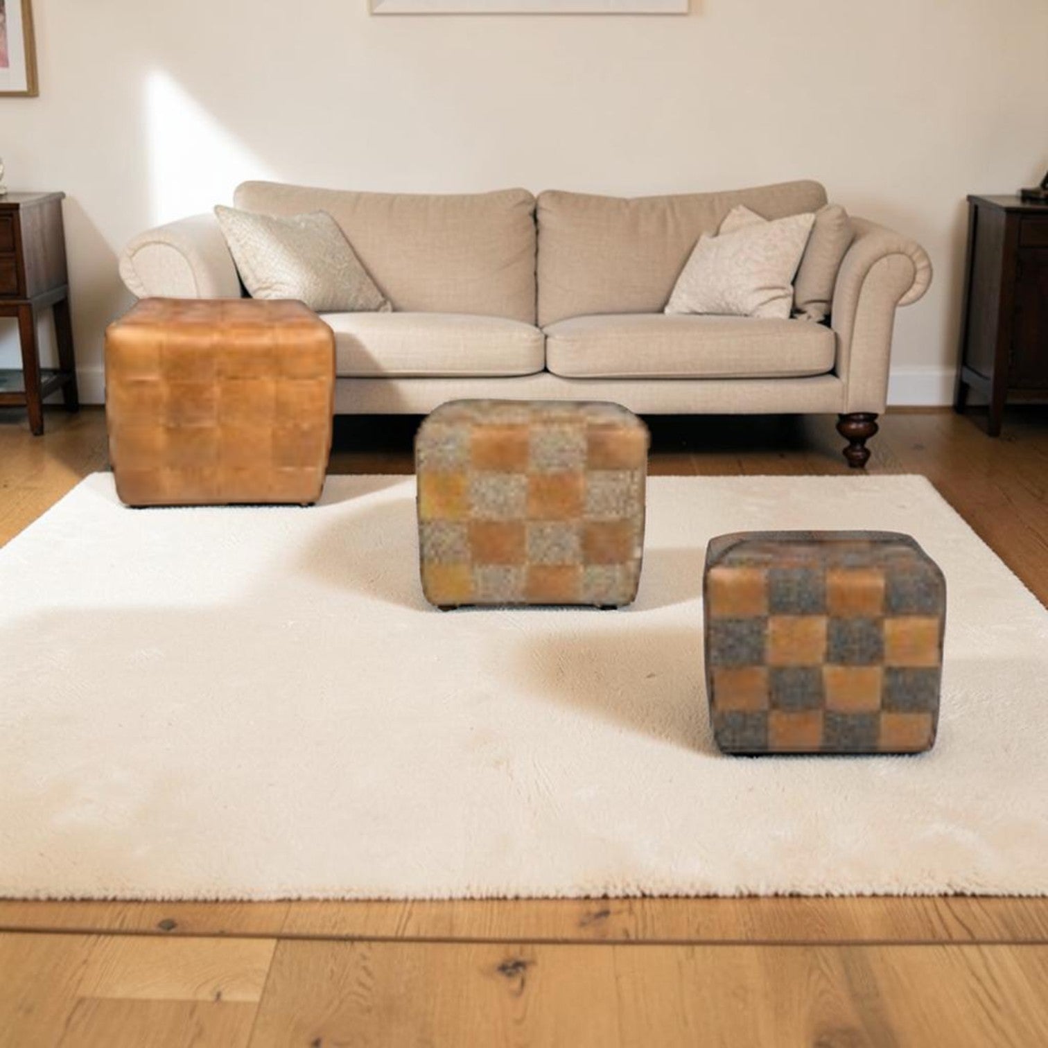 A styled living room scene featuring three square ottomans on a large cream shag rug over a light wood floor. The background shows a beige sofa with decorative pillows.