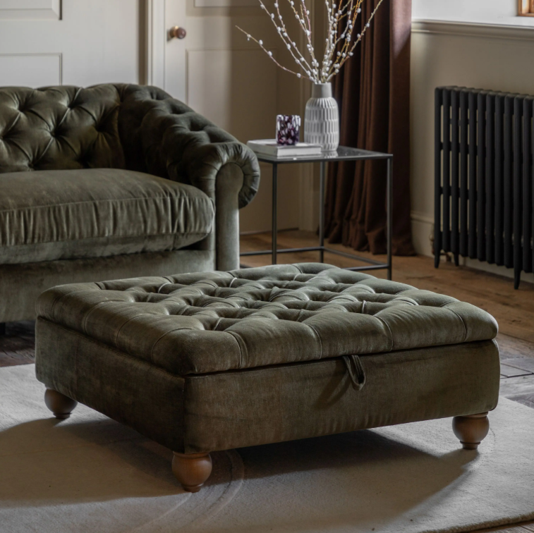 A large tufted storage ottoman in a muted olive green fabric, styled in a cozy living room next to a matching green sofa.