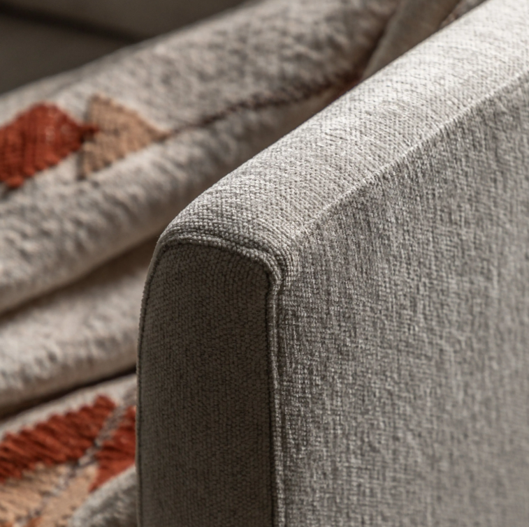 Close-up of Henley Natural upholstered armrest with a rounded corner, showing the fabric weave and a patterned textile in the background.
