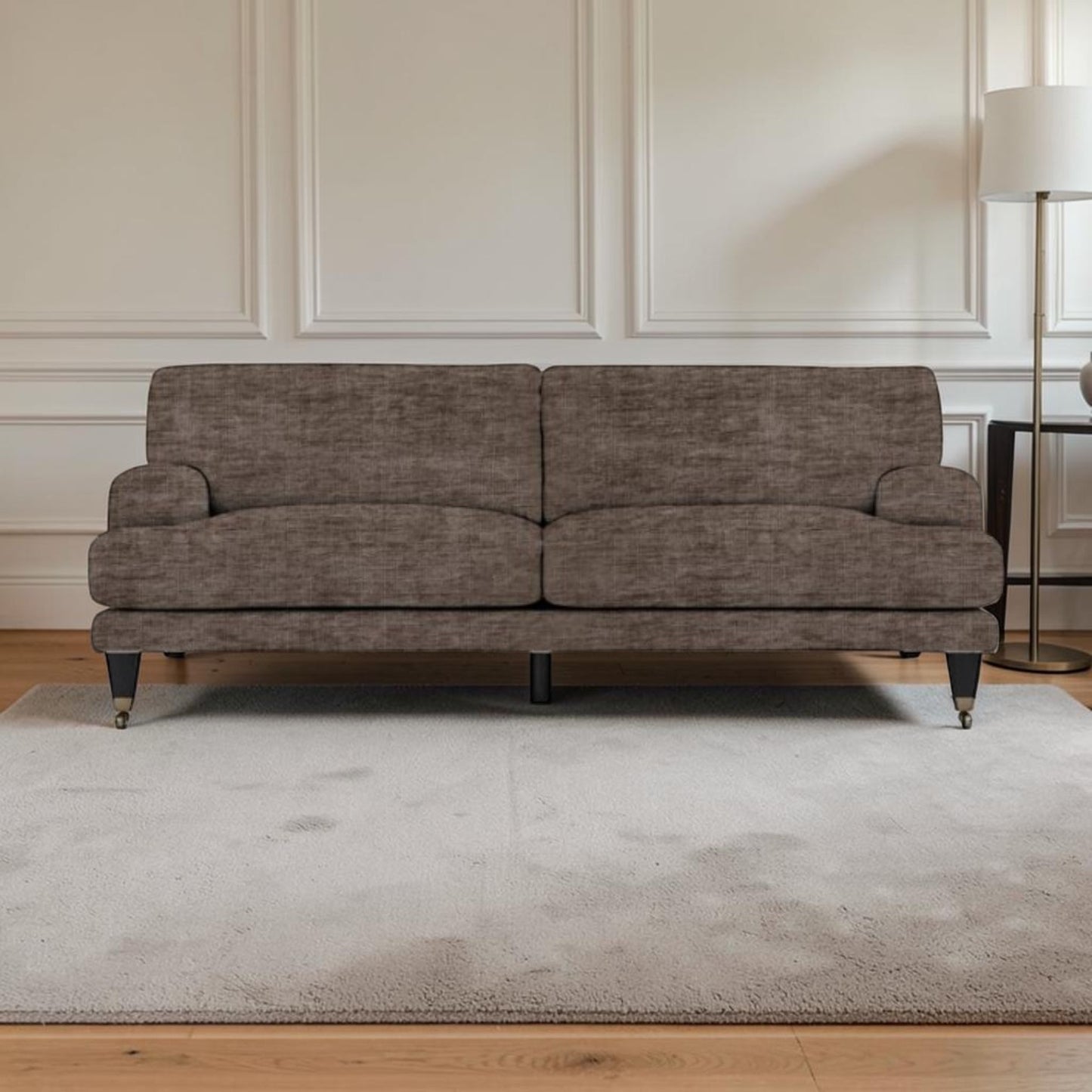 A upholstered sofa in textured taupe-brown fabric, shown in a styled living room setting with a light gray rug, wooden floor, white paneled wall, and a floor lamp.