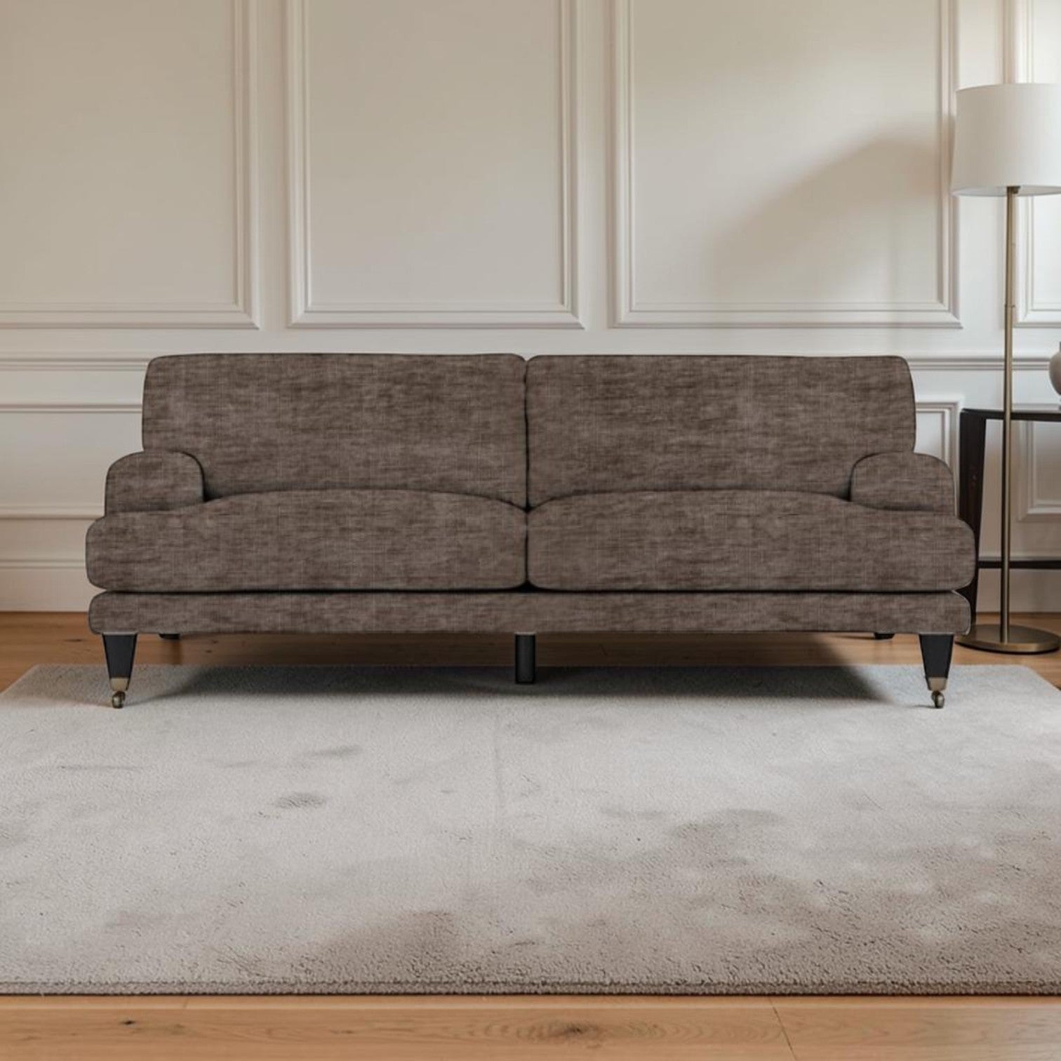 A upholstered sofa in textured taupe-brown fabric, shown in a styled living room setting with a light gray rug, wooden floor, white paneled wall, and a floor lamp.