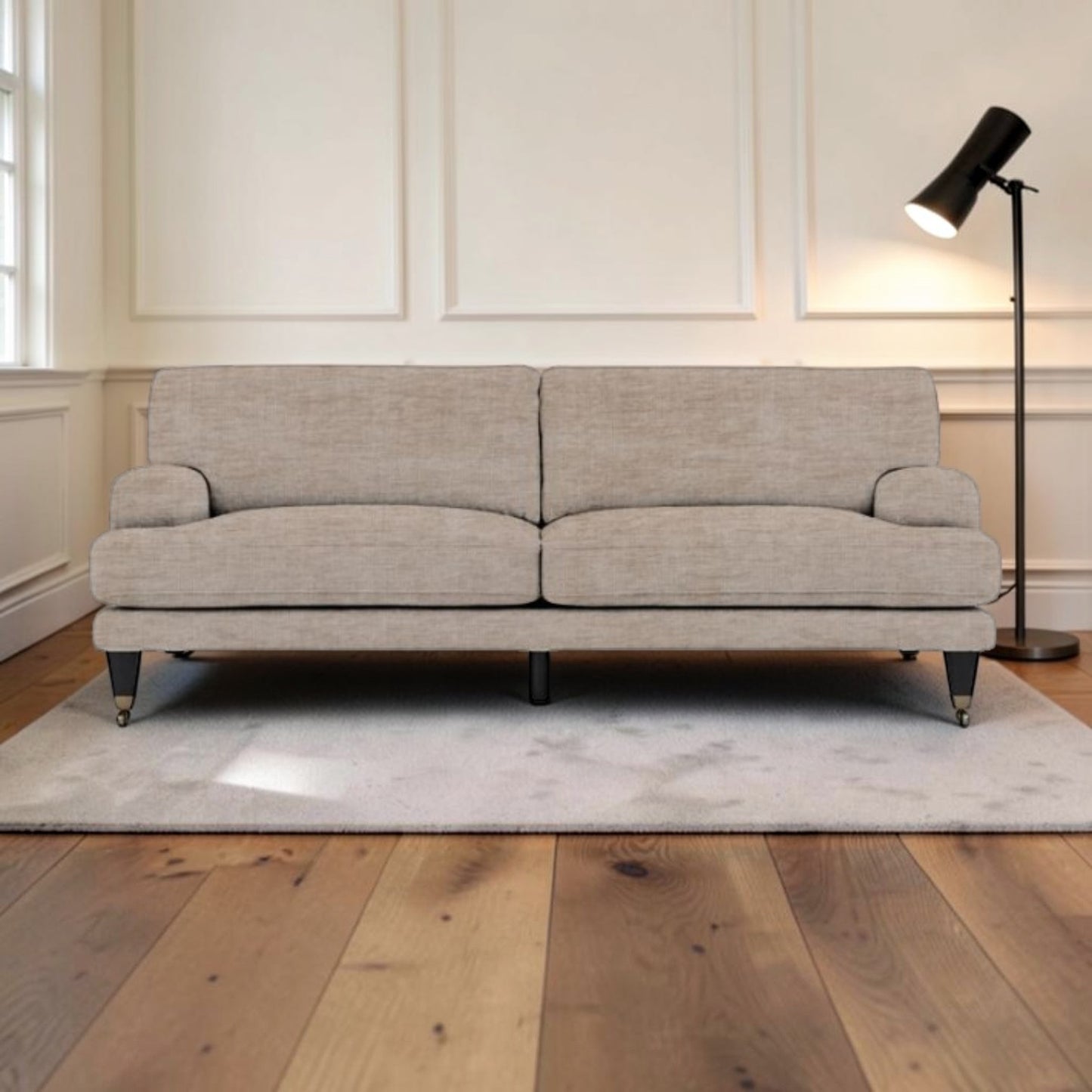 A light beige upholstered sofa with dark legs, placed on a white rug in a bright living room with wood floors and a black floor lamp.