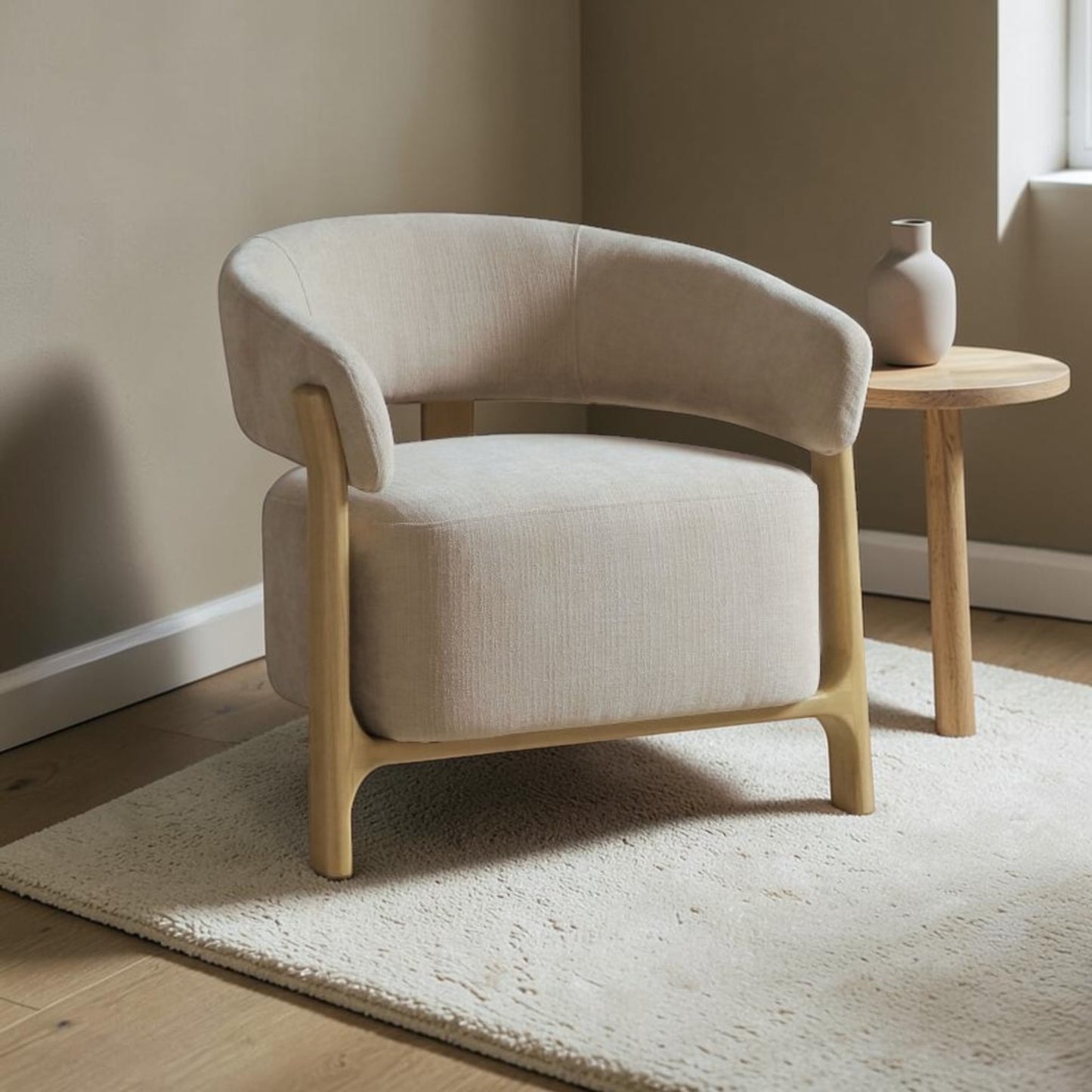 A modern barrel-style armchair with light beige textured upholstery and natural wood legs, styled in a minimalist room next to a small wooden side table.