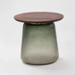 A small side table with a round dark brown wooden top and a tapered base featuring a green-to-beige gradient glaze, shown against a white background with a black border.