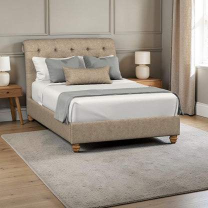A upholstered bed frame with a tufted headboard and matching footboard, shown in a styled bedroom setting with white bedding, gray pillows, bedside tables, lamps, curtains, and a light rug.