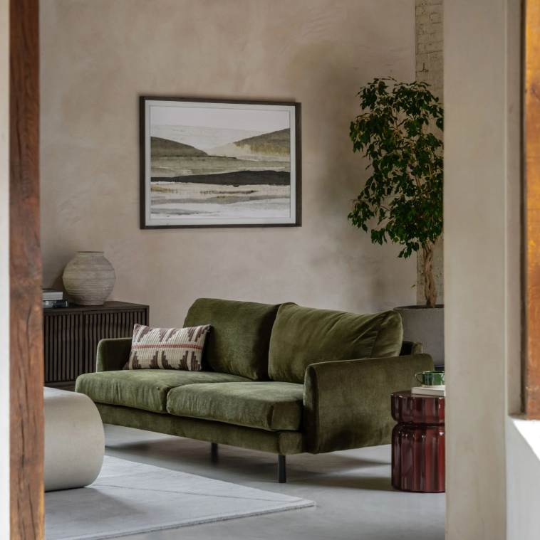 Green sofa in a living room with a painting on the wall and a plant.