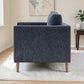 A side view of the Henley modern armchair upholstered in textured Charcoal fabric fabric with tapered wooden legs, shown in a styled living room setting on a white rug next to a side table.